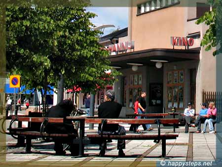 photo of two guys sitting on a bench in front of a movie house in Old Rauma